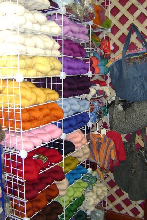 Wire shelving packed with colorful yarn beside hanging bags and garments