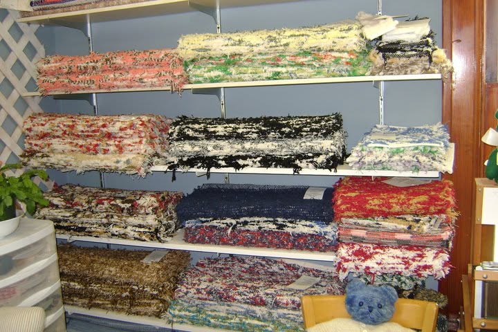 Shelves of colorful fringed textiles with a small blue knitted figure below