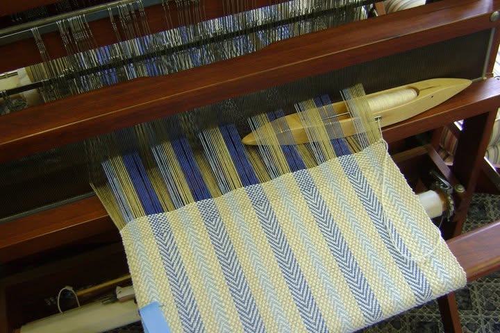 Blue-and-cream patterned weaving beneath warp threads and a wooden shuttle