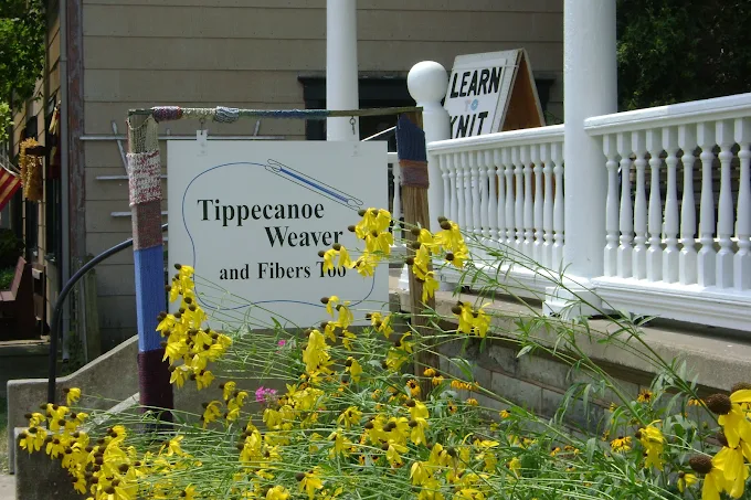 Shop sign beside a white porch railing and yellow flowers