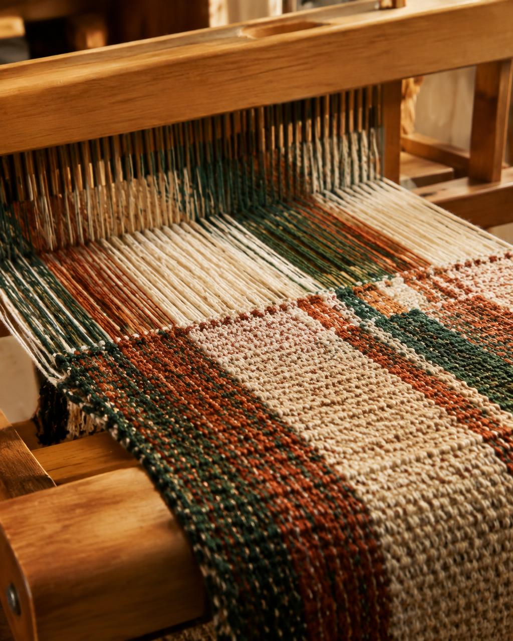 Close view of woven cloth in green, rust, and ivory on a wooden loom